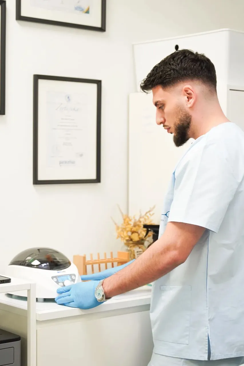 Mitarbeiter in hellblauer Arbeitskleidung und Handschuhen bereitet ein Gerät in einem Praxisraum vor.